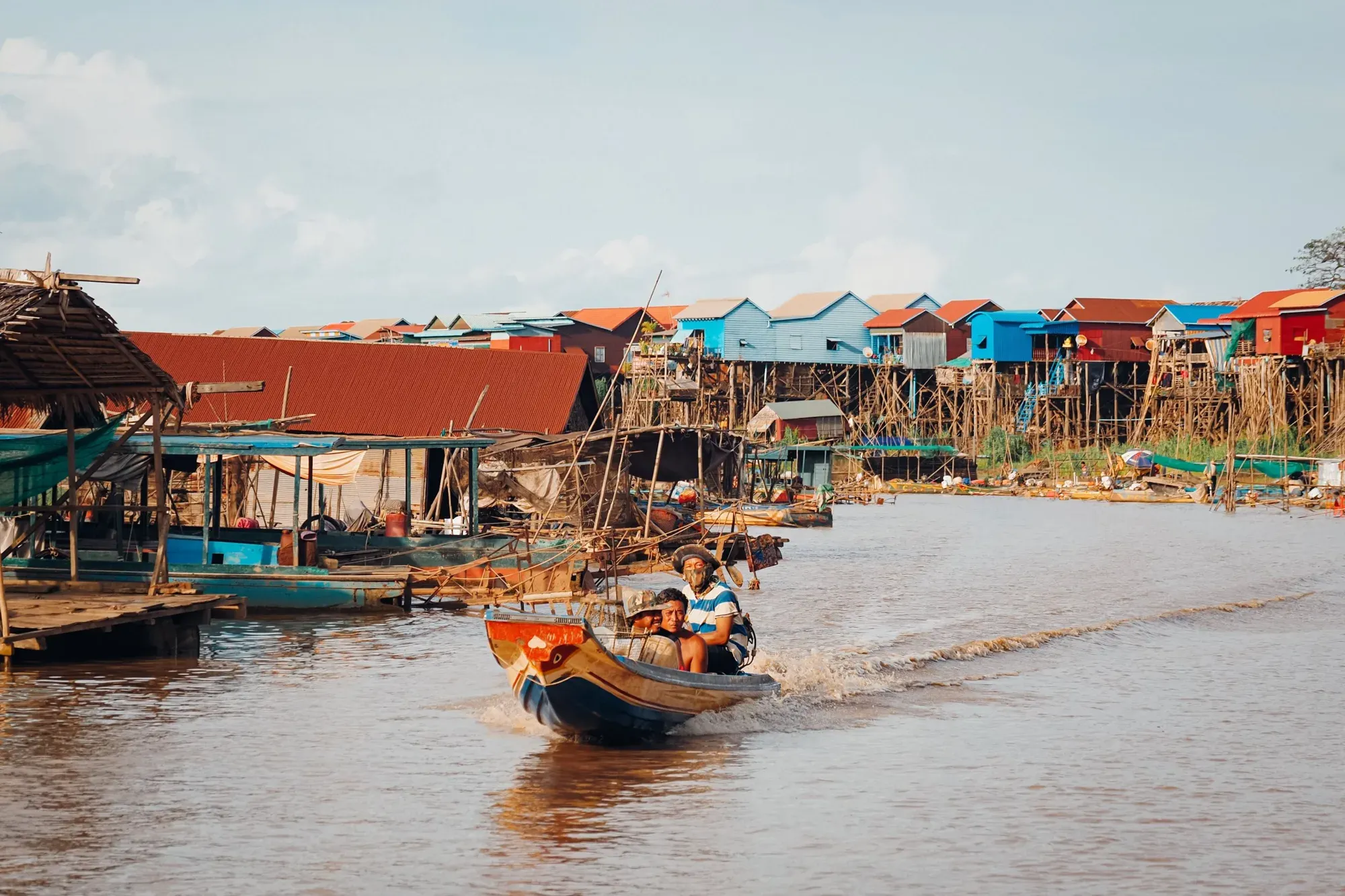 A boat heads up the channel past the stilt houses