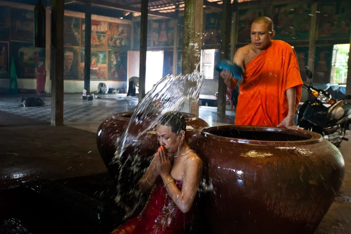 A monk pours water from a clay jar over a kneeling woman during a blessing at the pagoda