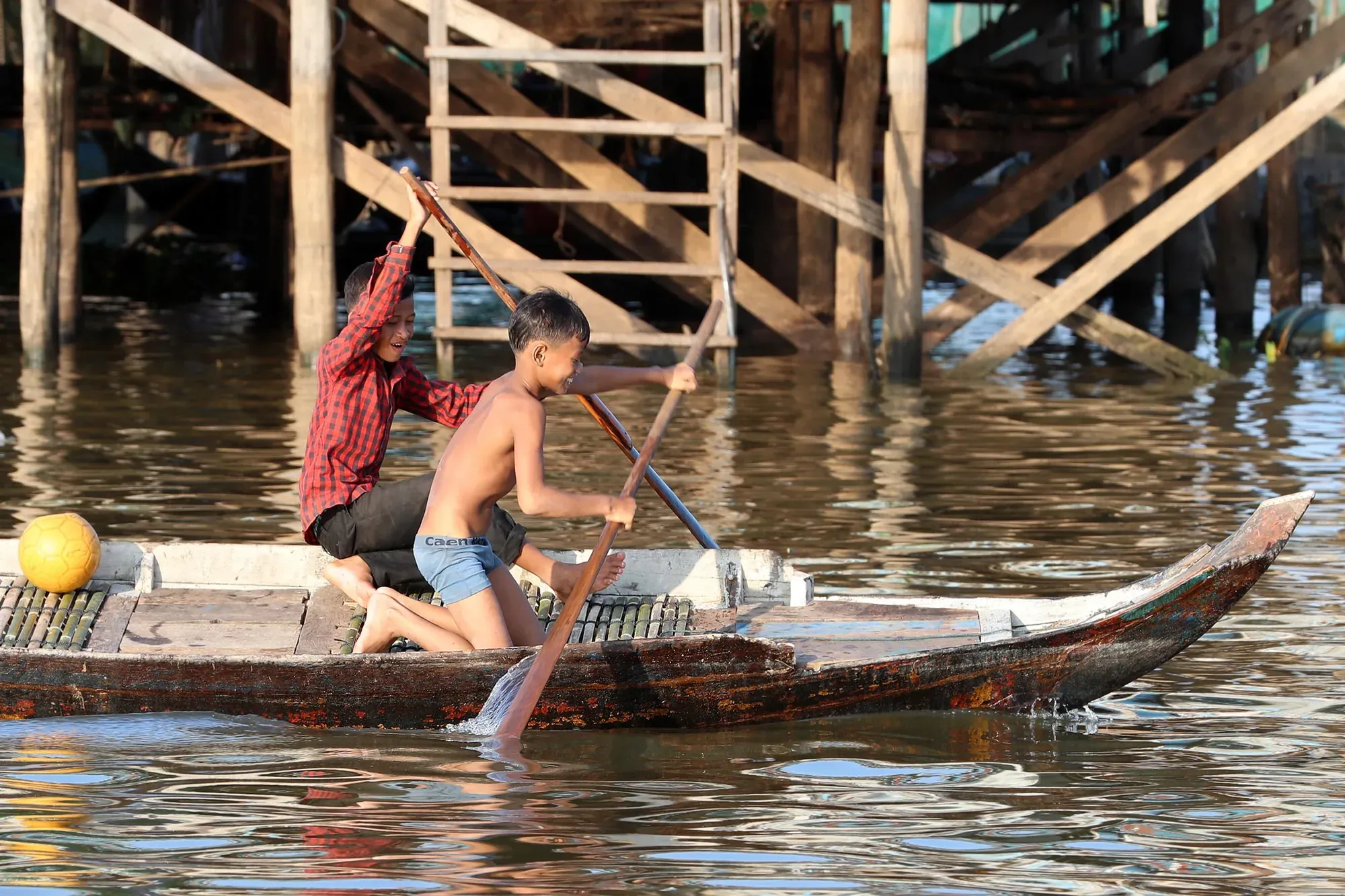 A woman rows a canoe beneath the stilt houses