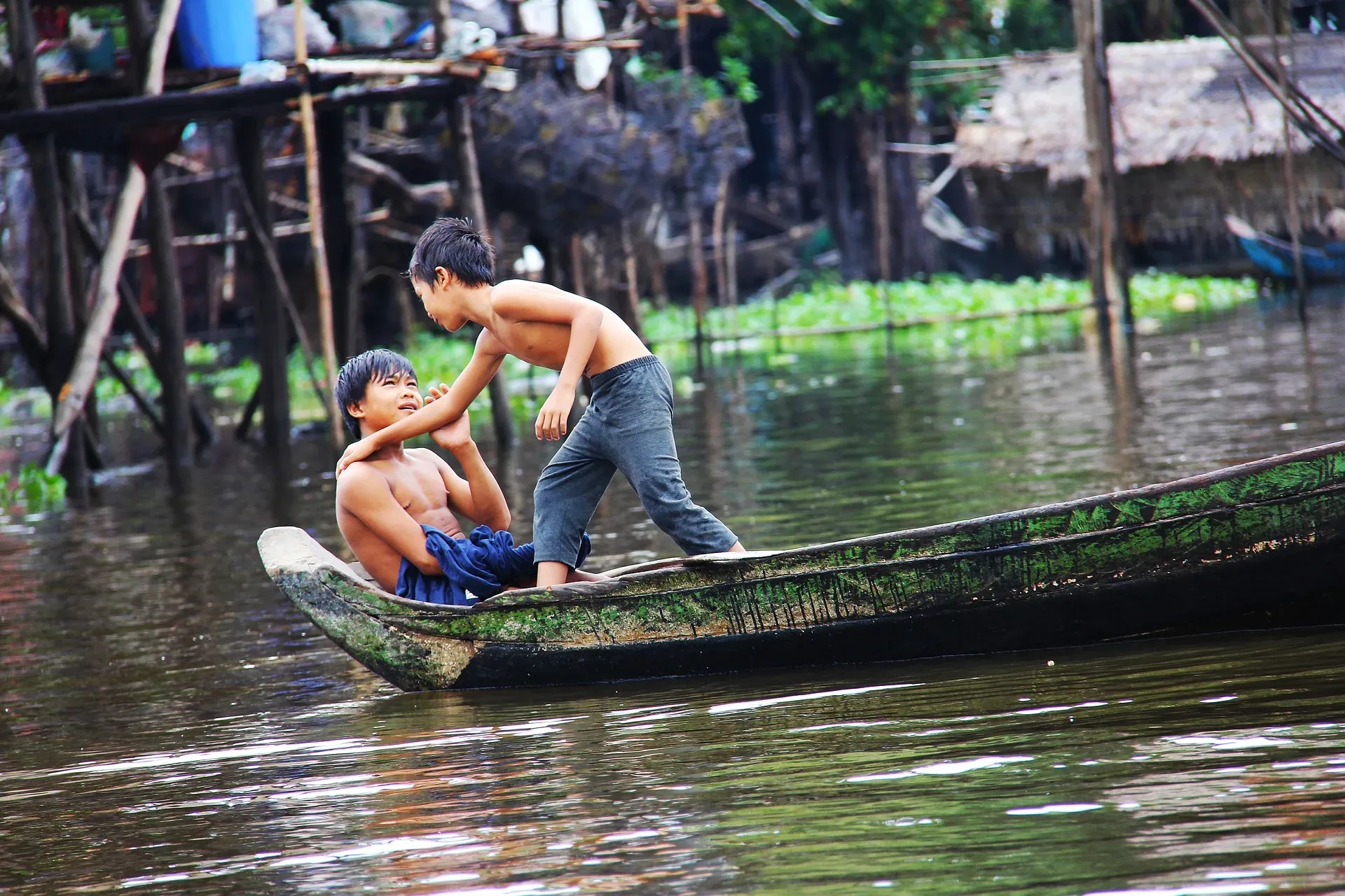 Children paddle a canoe between the stilt houses of Kompong Phluk