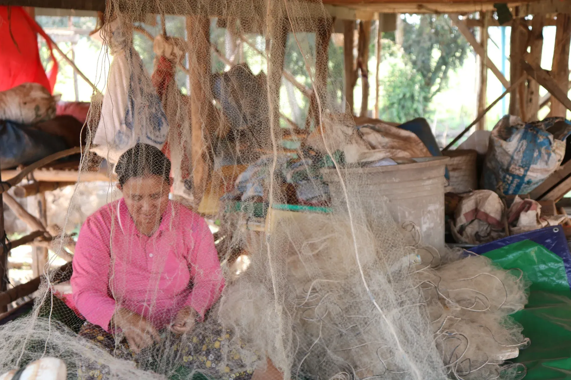 A woman mending fishing nets under her house